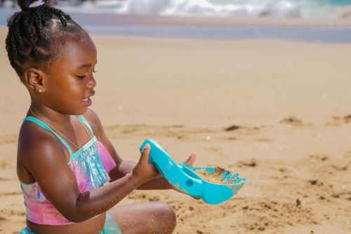 Young girl having fun on a sandy beach with a toy shovel, enjoying sunny day.