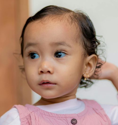Cute toddler looking curious while indoors in a pink dress.